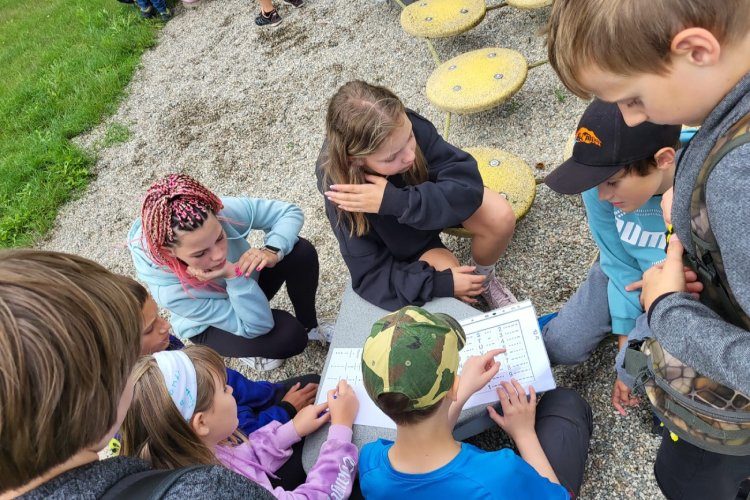 Děti se na venkovním hřišti zapojují do soutěže v luštění rébusů.